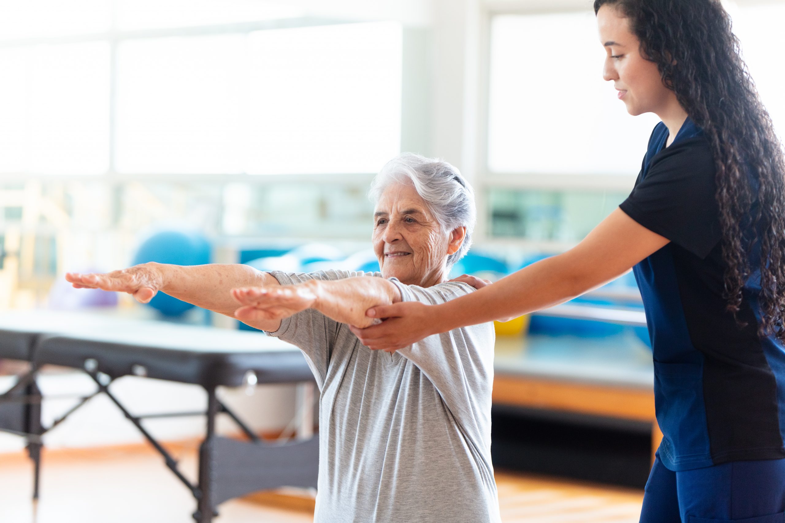 A Support worker assisting an elderly woman who is exercising
