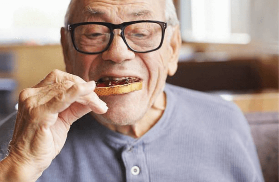An elderly man eating an open sandwich with jam