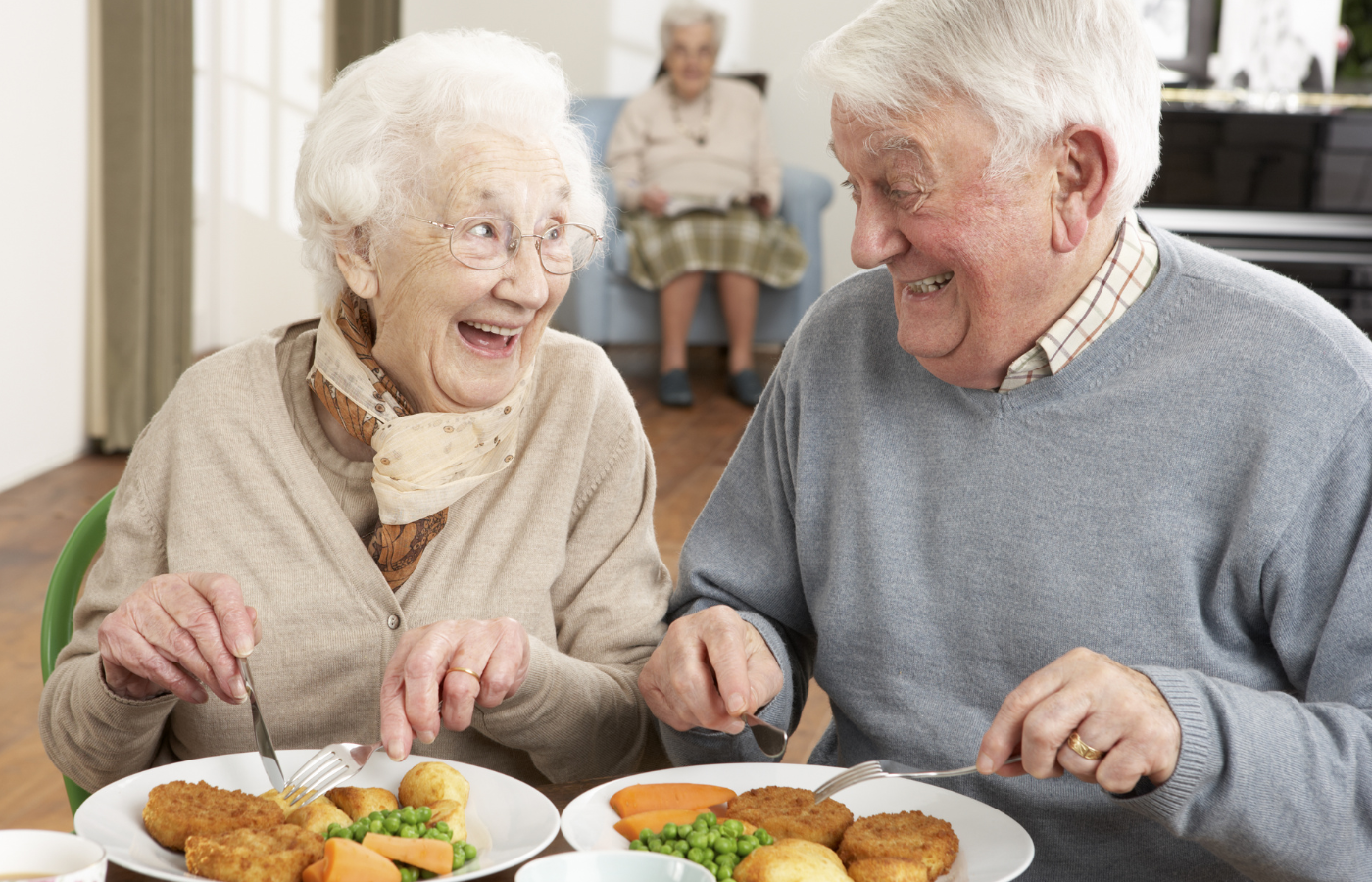 An elderly couple smiling and laughing while eating a meal